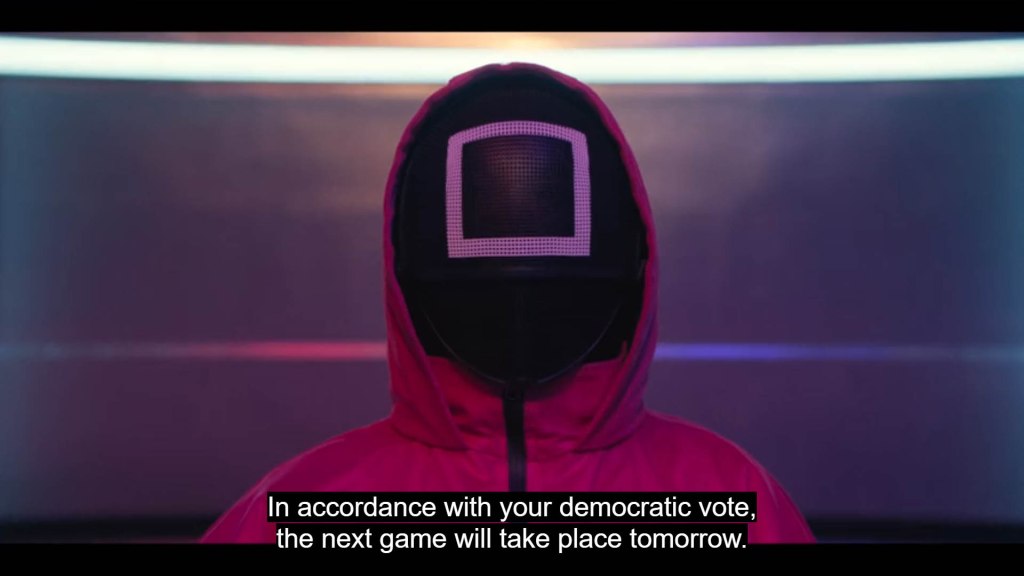 Squid Game manager explaining the democracy of voting 
"In accordance with your democratic vote,'
the next game will take place tomorrow."